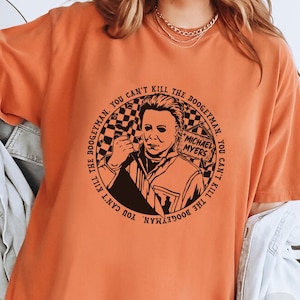May include: Orange t-shirt with a black and white graphic of Michael Myers from the Halloween franchise. The graphic features the text "You can't kill the boogeyman. You can't kill the boogeyman."