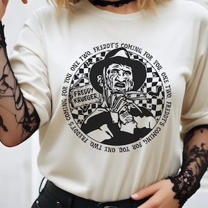 May include: White long-sleeve shirt with a black and white graphic print of Freddy Krueger from the movie A Nightmare on Elm Street. The graphic features the text "Freddy's Coming for You. One Two, Freddy's Coming for You. One Two, Freddy's Coming for You."