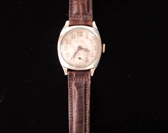 May include: A vintage wristwatch with a white face and black Roman numeral hour markers. The watch has a gold-tone case and a brown leather strap.