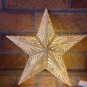 May include: A white, paper star with a cut-out design, illuminated from within. The star is hanging from a brick wall.