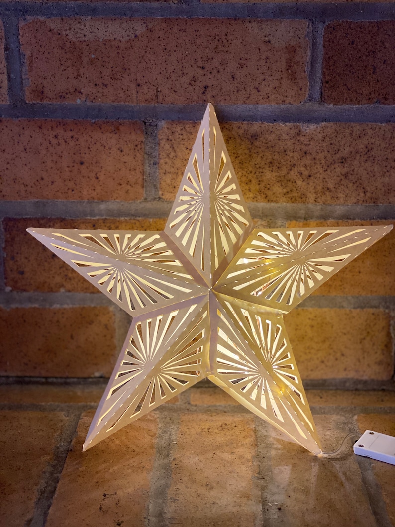 May include: A white, paper star with a cut-out design, illuminated from within. The star is hanging from a brick wall.
