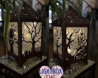 Puede incluir: Una caja de luz de madera marrón con una escena de Halloween espeluznante. La escena incluye un árbol con ramas desnudas, una casa encantada y calabazas. La caja de luz está iluminada desde el interior, creando un brillo cálido. El texto "LIGHTBOX SVG" es visible en la parte frontal de la caja de luz.