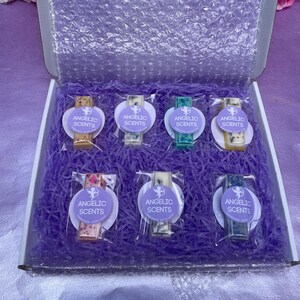 May include: An open box containing seven individually wrapped wax melts in various colours, nestled in purple shredded paper. Each melt has a label reading "ANGELIC SCENTS". The box is lined with bubble wrap.