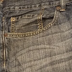 May include: Close-up of blue denim jeans with a classic five-pocket design. The jeans feature a button and zipper closure, belt loops, and rivets. The tag reads "42 x 32". The denim has a worn, faded appearance.