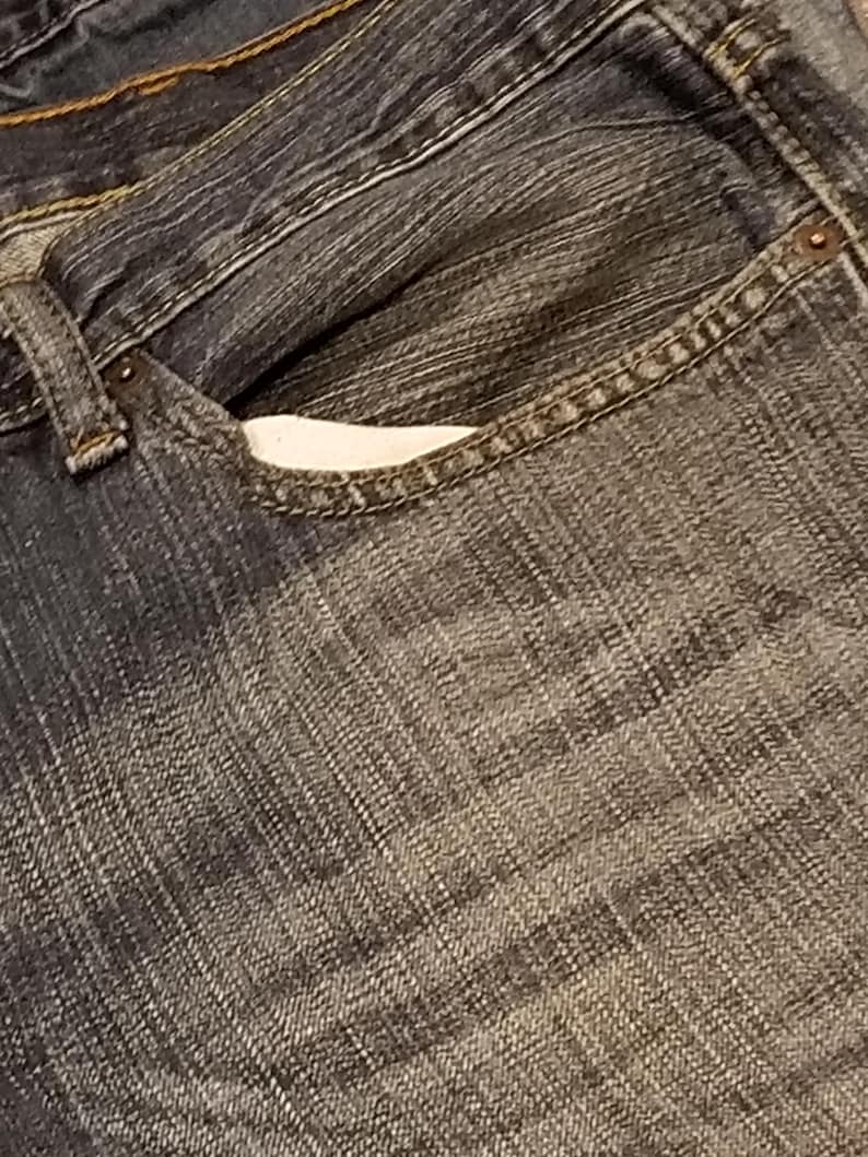 May include: Close-up of a pair of blue denim jeans. The image focuses on the front pocket, showing the stitching and the texture of the denim fabric. The jeans have a classic, worn look.