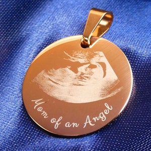 Könnte beinhalten: Ein goldfarbener Anhänger mit einem gravierten Ultraschallbild und dem Text "Mom of an Angel".