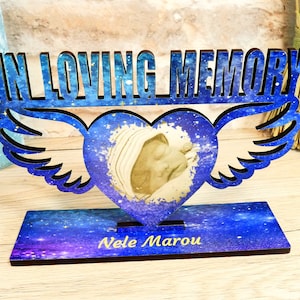 Könnte beinhalten: Holzgedenkplakette mit einem blauen Galaxie-Design. Die Plakette hat einen herzförmigen Ausschnitt mit einem Foto eines Babys darin. Der Text "IN LOVING MEMORY" befindet sich oben auf der Plakette und der Name "Nele Marou" unten.