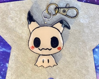 May include: A beige and black cartoon ghost character keychain with a silver and gold metal clasp. The ghost has black eyes, a black mouth, and red cheeks.
