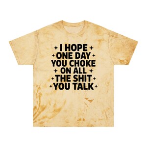 Op de afbeelding: Een t-shirt met korte mouwen en een beige en bruin tie-dye patroon. In het midden staat zwarte tekst: I HOPE ONE DAY YOU CHOKE ON ALL THE SHIT YOU TALK, geaccentueerd door kleine zwarte vierpuntige sterren aan de zijkanten.