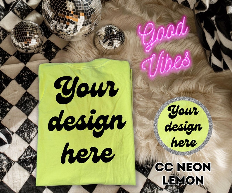 Op de afbeelding: Een neon-geel T-shirt met de tekst "Your design here" in zwart. Het shirt ligt op een wit, pluche oppervlak met een zilveren cirkel waarop "Your design here" en de tekst "CC NEON LEMON" staat.