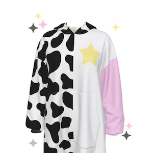 Pode incluir: Um moletom branco com estampa de vaca preta e branca de um lado e uma estrela rosa e amarela do outro.