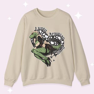 Op de afbeelding: Beige sweatshirt met een hartvormige afbeelding met de tekst "Lusty Argonian Maid". De afbeelding toont een groen hagedisachtig personage in een dienstmeisjesoutfit. Het ontwerp bevat zwart-witte accenten en kleine vlinderdetails.