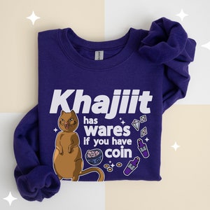 Op de afbeelding: Paarse trui met een witte afbeelding van een bruine kat met de tekst "Khajiit has wares if you have coin".