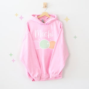 May include: Pink hoodie with a white graphic of the word "Mochi" and three pastel-colored mochi balls.