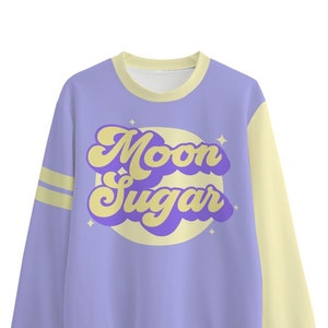 Op de afbeelding: Een lavendelkleurig en geel sweatshirt met een retro-stijl grafische afbeelding met de tekst "Moon Sugar" in paarse en gele letters.