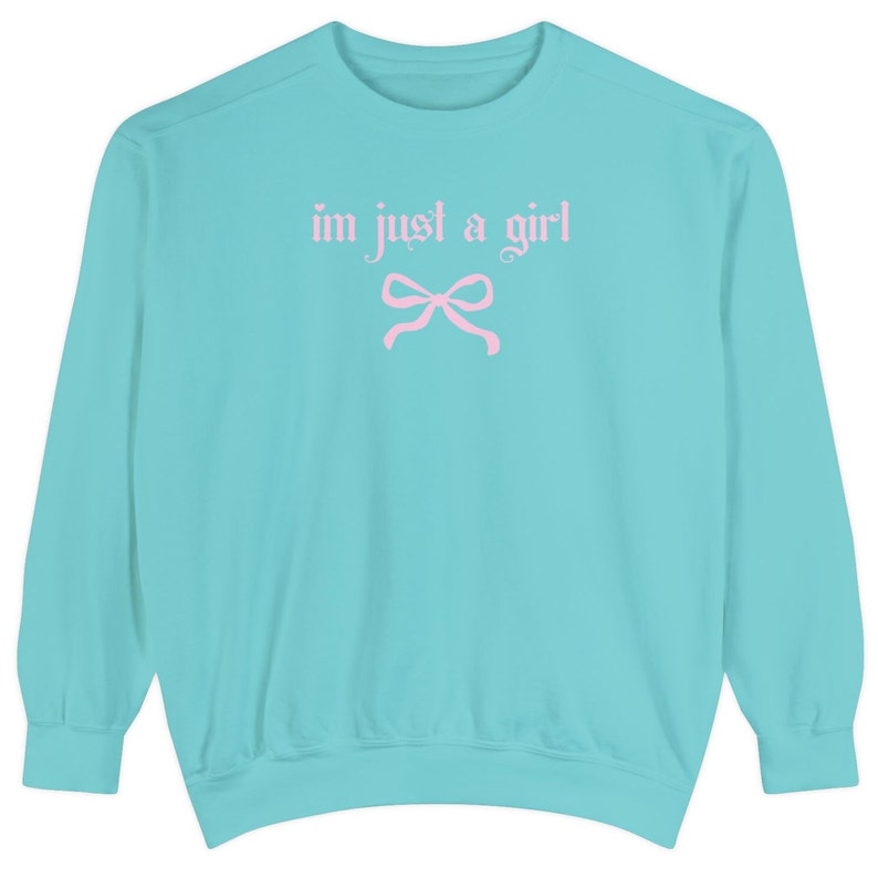 Op de afbeelding: Een turquoise blauwe trui met de tekst "i'm just a girl" in roze letters en een roze strik.