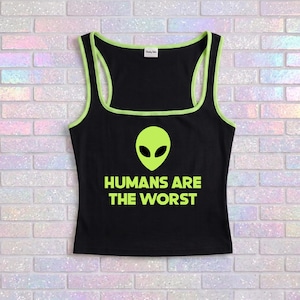 Könnte beinhalten: Schwarzes Tanktop mit neongrünen Zierleisten und einem Alien-Motiv. Der Text "HUMANS ARE THE WORST" ist in Neongrün unter dem Alien-Motiv aufgedruckt. Das Tanktop hat einen quadratischen Ausschnitt.
