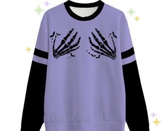 May include: A lavender sweatshirt with black long sleeves and a black stripe across the shoulders. The front of the sweatshirt has a graphic of two skeleton hands with fingers pointing towards each other.