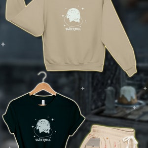 May include: A set of gamer gifts featuring a beige sweatshirt, a black t-shirt, and a pair of beige shorts. All three items feature a cartoon image of a sweet roll with the text "Sweetroll".