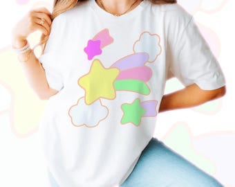 May include: White t-shirt featuring a colourful cartoon design of a shooting star with clouds and stars. The design is in shades of pink, yellow, green, and purple.