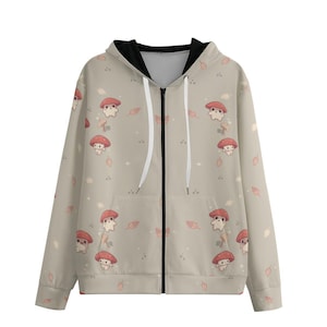 May include: A beige zip-up hoodie with a repeating pattern of cartoon mushrooms with red caps and small leaves. The hoodie has a black interior lining in the hood and a white zipper with white drawstrings.