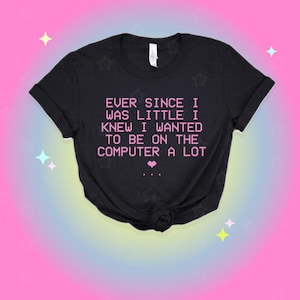 May include: A black short-sleeved t-shirt featuring the pink pixelated text: EVER SINCE I WAS LITTLE I KNEW I WANTED TO BE ON THE COMPUTER A LOT, followed by a small pink heart and three dots. The shirt has a crew neckline and a standard fit.