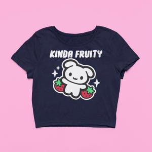 Op de afbeelding: Marineblauwe crop top met de tekst "Kinda Fruity" boven een wit cartoonfiguur dat twee rode aardbeien vasthoudt. Witte sterren staan aan weerszijden van het figuur.