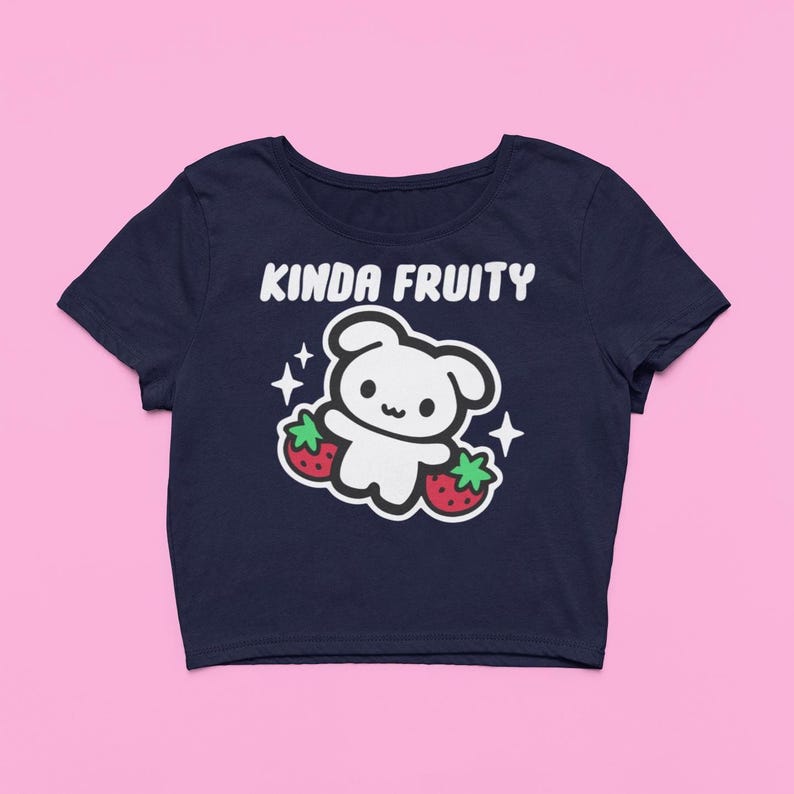 Op de afbeelding: Marineblauwe crop top met de tekst "Kinda Fruity" boven een wit cartoonfiguur dat twee rode aardbeien vasthoudt. Witte sterren staan aan weerszijden van het figuur.