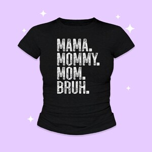 May include: A black short-sleeved t-shirt featuring white distressed-style text printed on the front. The text is stacked in four lines and reads: MAMA. MOMMY. MOM. BRUH. The shirt has a crew neckline and a standard fit, presented against a light purple background.