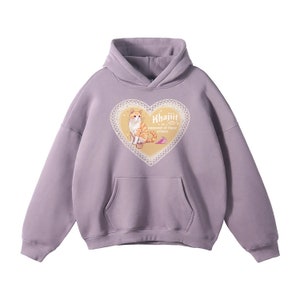 Op de afbeelding: Een lavendelkleurige hoodie met een kangoeroezak en een capuchon met trekkoord. De voorkant heeft een hartvormig ontwerp met een kattenillustratie en de tekst "Khajiit is innocent of these crimes."