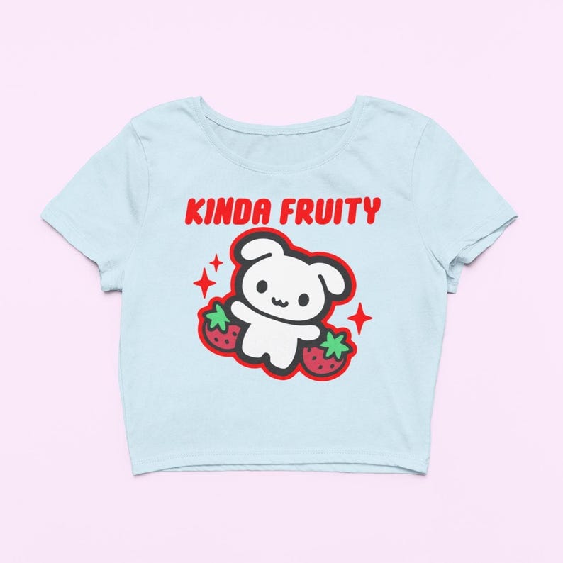 Op de afbeelding: Lichtblauw crop top met de rode tekst "Kinda Fruity". Het ontwerp bevat een witte cartoonbeer, twee aardbeien en rode steraccenten. Deze top is een casual item. Het shirt is een casual, alledaags kledingstuk.