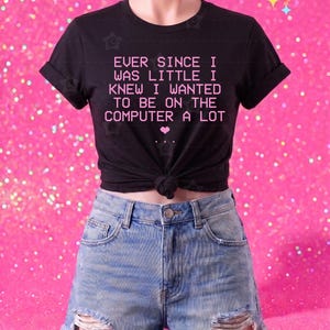 May include: A black short-sleeved t-shirt with a knotted hem featuring the pink text "EVER SINCE I WAS LITTLE I KNEW I WANTED TO BE ON THE COMPUTER A LOT" and a small pink heart, paired with light blue distressed denim shorts with a frayed hem.