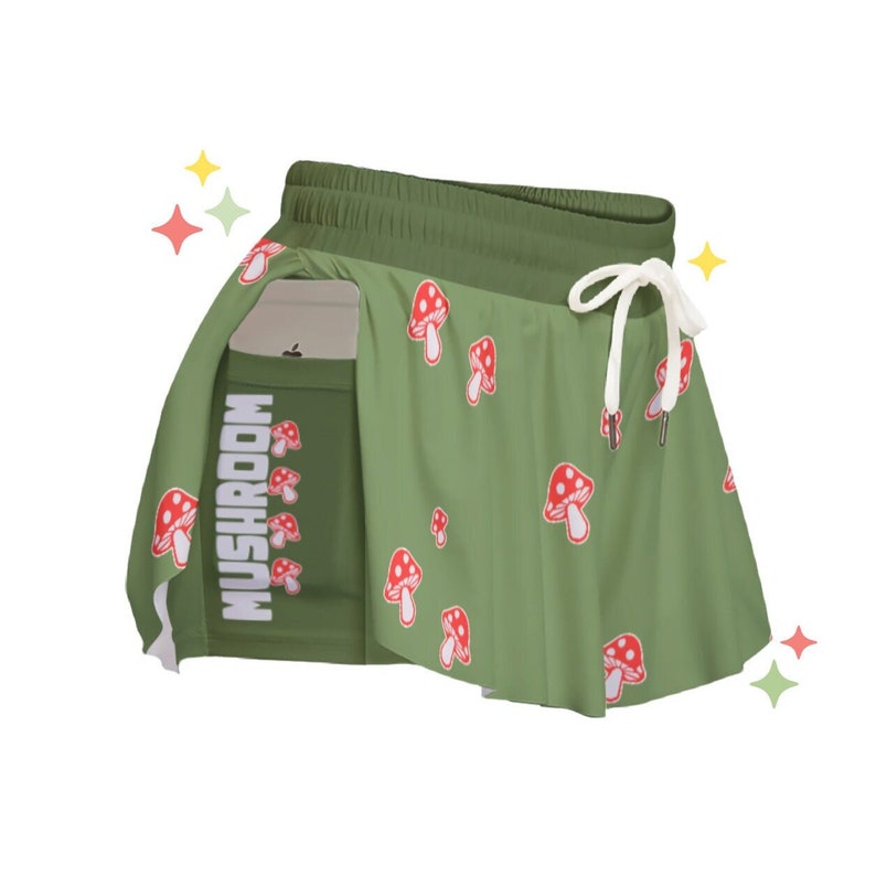 May include: Green athletic shorts with a mushroom print and the word "MUSHROOM" on the side. The shorts have a built-in skirt.