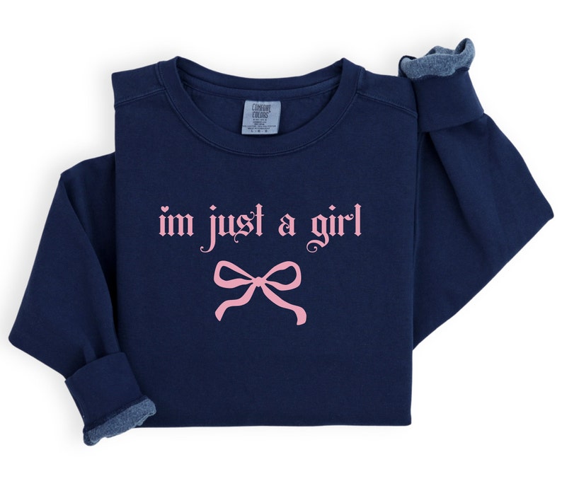 Op de afbeelding: Navyblauwe trui met een roze strik en de tekst "i'm just a girl" in gotische letters.