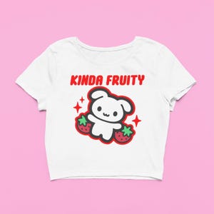 Op de afbeelding: Witte crop top met een rode en zwarte afbeelding. De afbeelding toont een schattig, beerachtig karakter met twee aardbeien en de tekst "KINDA FRUITY" in het rood. Het ontwerp bevat rode steraccenten.