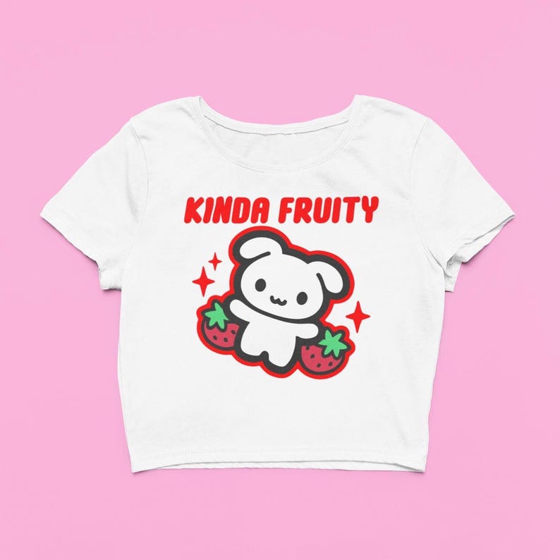 Op de afbeelding: Witte crop top met een rode en zwarte afbeelding. De afbeelding toont een schattig, beerachtig karakter met twee aardbeien en de tekst "KINDA FRUITY" in het rood. Het ontwerp bevat rode steraccenten.