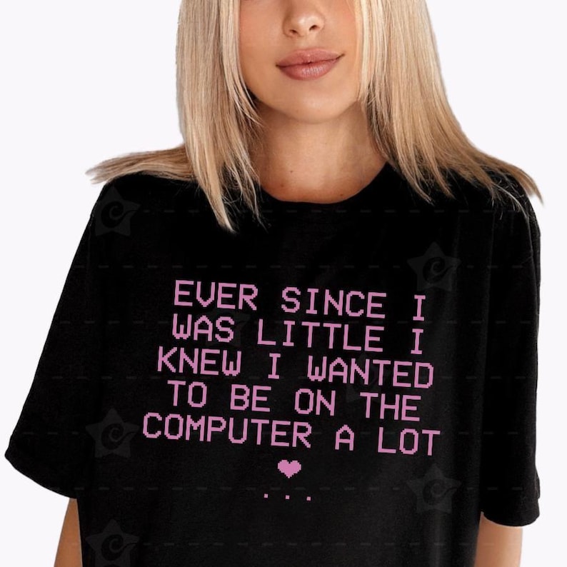 May include: A black short-sleeved t-shirt featuring the light pink pixelated text: EVER SINCE I WAS LITTLE I KNEW I WANTED TO BE ON THE COMPUTER A LOT, followed by a small pink pixelated heart and three dots centered below the text.
