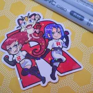 May include: A holographic sticker featuring the Team Rocket trio from the Pokemon anime. The sticker is red with a large letter R in the center. Jessie, James, and Meowth are depicted in a cartoon style. The sticker has a glittery finish.
