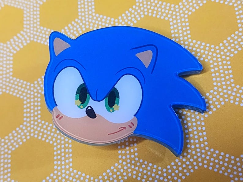 May include: A blue and brown cartoon character with green eyes and a mischievous expression. The character has a blue spiky mohawk and a white muzzle. The character is a popular video game character.