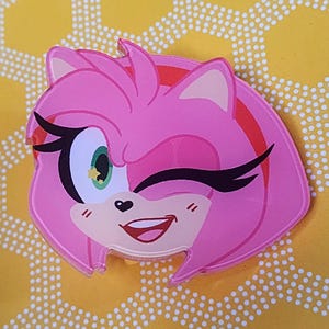 May include: Pink cartoon character with a winking eye and a big smile. The character has a heart-shaped nose and pink hair.