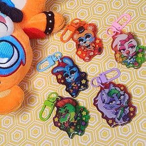 Puede incluir: Seis llaveros coloridos con personajes de dibujos animados con un tema de rock and roll. Cada llavero tiene un personaje diferente con un diseño y una combinación de colores únicos. Los llaveros están hechos de plástico transparente con un acabado brillante.