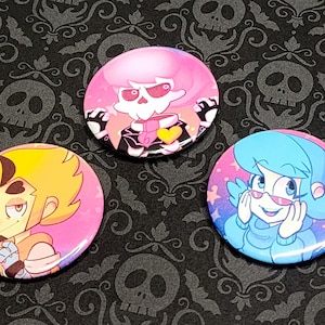 Puede incluir: Tres botones redondos con personajes de dibujos animados. El primer botón presenta un esqueleto de pelo rosa con un atuendo blanco y negro y un corazón amarillo. El segundo botón presenta un personaje de pelo amarillo con un fondo rosa. El tercer botón presenta un personaje de pelo azul con un fondo rosa y azul.