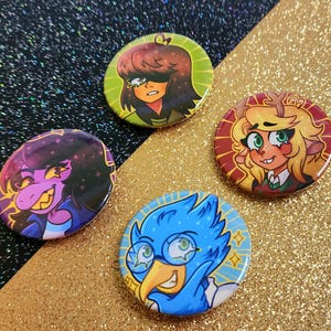 May include: Four colorful round buttons with cartoon character illustrations. The buttons feature characters with various hair colors and expressions, set against green, red, and blue backgrounds. The buttons are on a gold and black glitter surface.