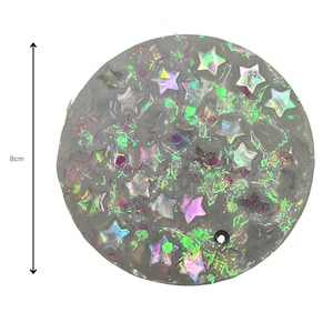 May include: A round, clear, 8 cm diameter resin coaster with iridescent glitter and star shapes embedded in the resin.
