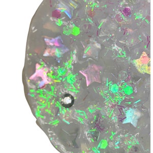 May include: A clear slime with iridescent glitter and star-shaped confetti. The slime is a light gray color and has a smooth, glossy finish.