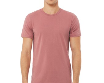 May include: A short-sleeved, crew neck t-shirt in a muted rose color. The shirt is made of a soft material and has a classic, casual style. The model is wearing blue jeans.