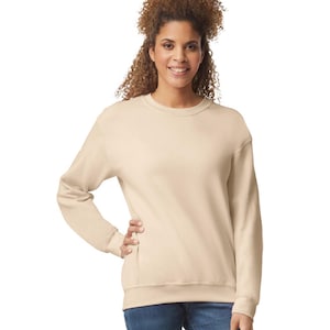 May include: A beige crew neck sweatshirt with long sleeves. The sweatshirt is a solid color and has ribbed cuffs and hem. The model is wearing blue jeans.