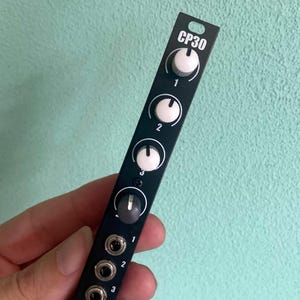 Puede incluir: Módulo electrónico negro con la inscripción "CP30", perillas blancas y conectores de entrada. El módulo tiene cuatro perillas blancas y una perilla gris, cada una numerada. El módulo tiene tres conectores de entrada numerados 1, 2 y 3.