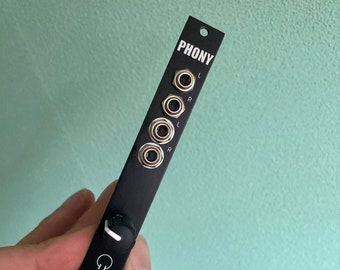 May include: Black metal audio interface with the word "PHONY" printed on the front. It has four jacks and a knob with a white line.