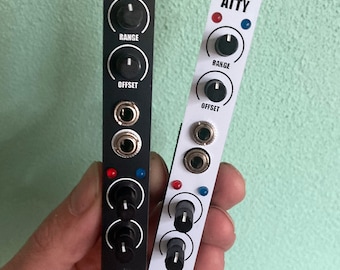 May include: Two black and white ATTTY modules for electronic music production. Each module has a red and blue LED, two knobs labeled "RANGE" and "OFFSET", and three jacks. The modules are held in a hand.